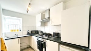 A modern kitchen with white cabinets, a black countertop, a microwave, a stove, and a refrigerator. - The County Staycation (Liverpool)