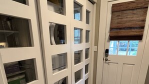Ein Flur mit einer weißen Tür, einem Fenster mit Jalousien und einem Teppichboden.