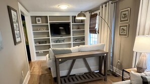 Ein Wohnzimmer mit einer Couch, einem Couchtisch, einem Fernseher und einem Bücherregal.