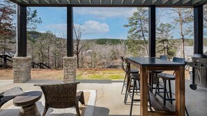 Eine Terrasse im Freien mit Tisch, Stühlen, Steinpfeilern und Blick auf ein bewaldetes Gebiet.