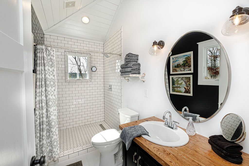 A modern bathroom with a shower, toilet, and sink, featuring a wooden vanity and a large mirror.