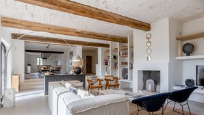 Een ruime woonkamer met een open haard, houten balken en een moderne bank.