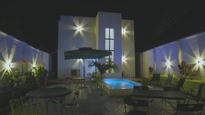 An outdoor patio with a pool, chairs, and tables.