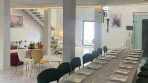 A conference room with a long table set for a meeting, surrounded by chairs. There is a staircase leading to another level and a kitchen area in the background.