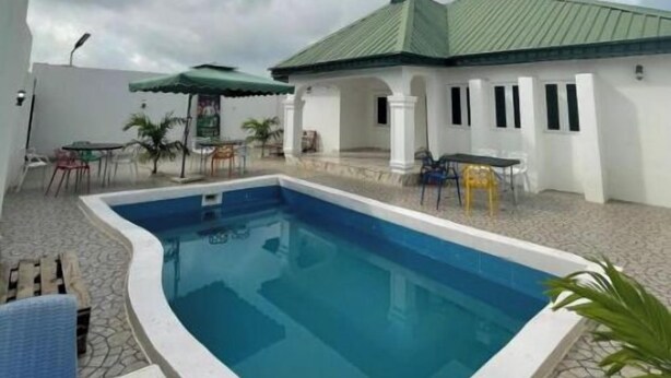 A swimming pool with a tiled deck, surrounded by outdoor seating and a covered area.