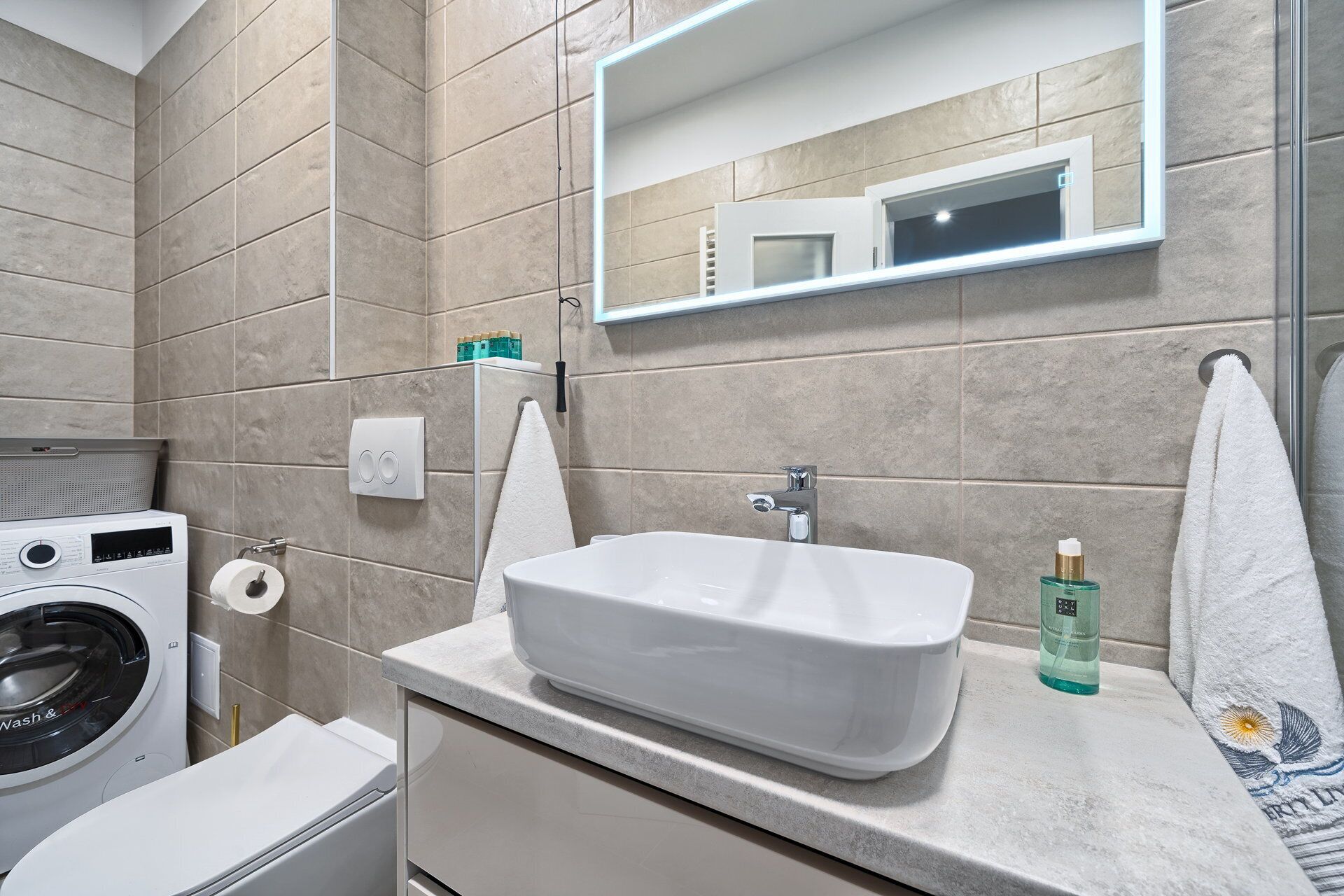 A modern bathroom with a built-in washing machine, a sink, and a mirror.