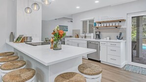 Een moderne keuken met een centraal eiland, witte kasten en een eethoek met krukken.