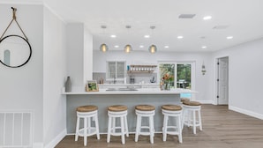 Een moderne keuken met een centraal eiland, barkrukken, hanglampen en uitzicht op de omgeving.