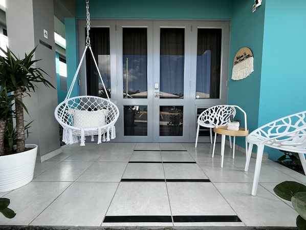 A modern entrance with a swing chair, white chairs, and a potted plant.