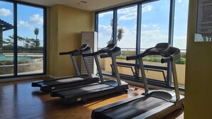 A gym with three treadmills, large windows, and a view of a pool and palm trees.