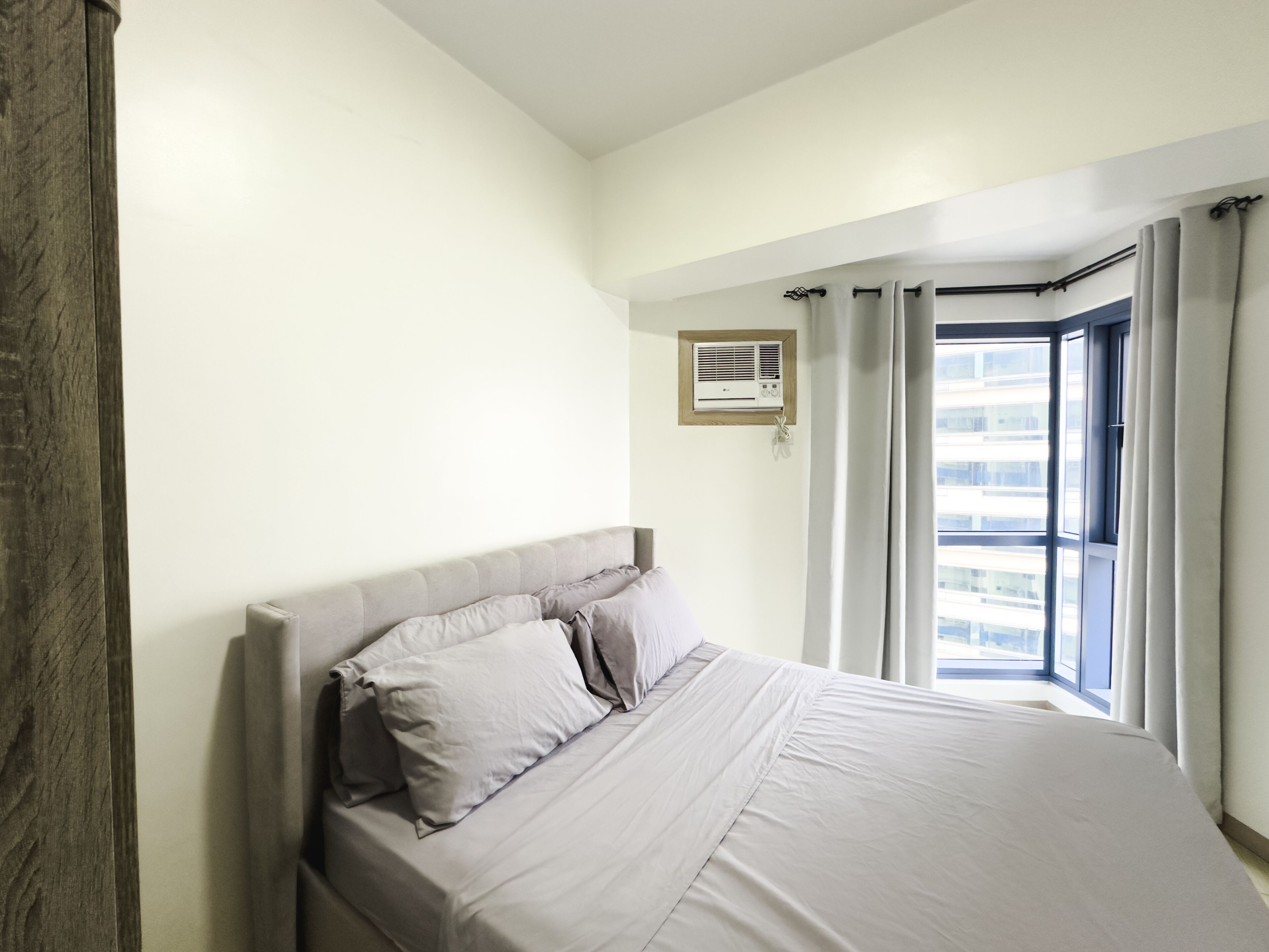 A bedroom with a large bed, a window with curtains, and an air conditioning unit on the wall.