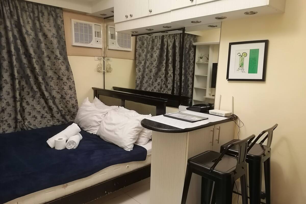 A compact hotel room with a single bed, a small desk with a chair, a mirror, and a framed picture on the wall.