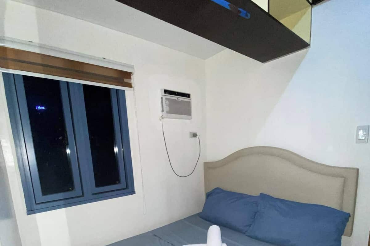 A bedroom with a bed, a window, and an air conditioning unit.