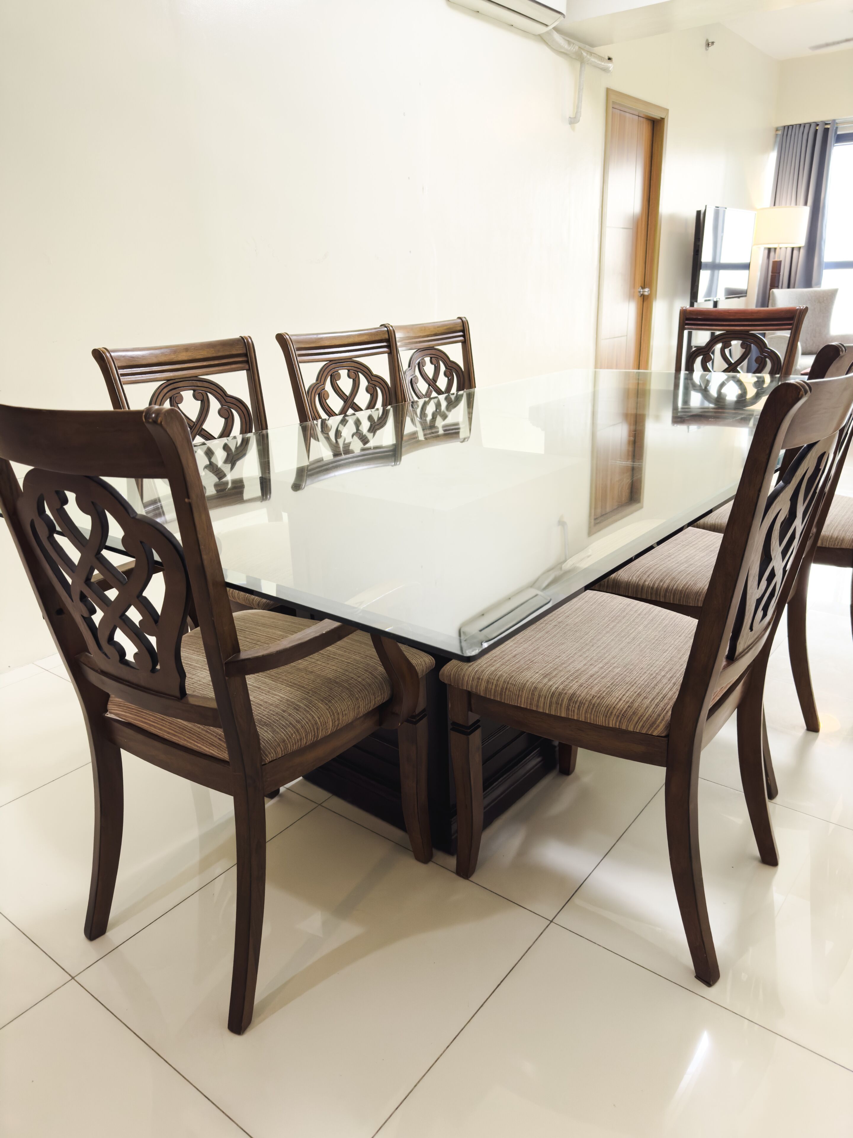 A dining area with a glass-top table surrounded by wooden chairs with cushioned seats.