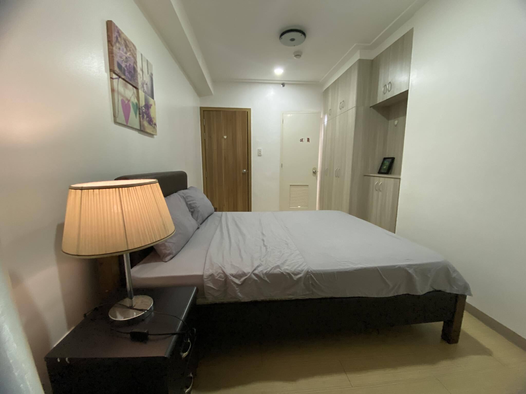 A bedroom with a bed, a bedside table with a lamp, a wardrobe, and a door.