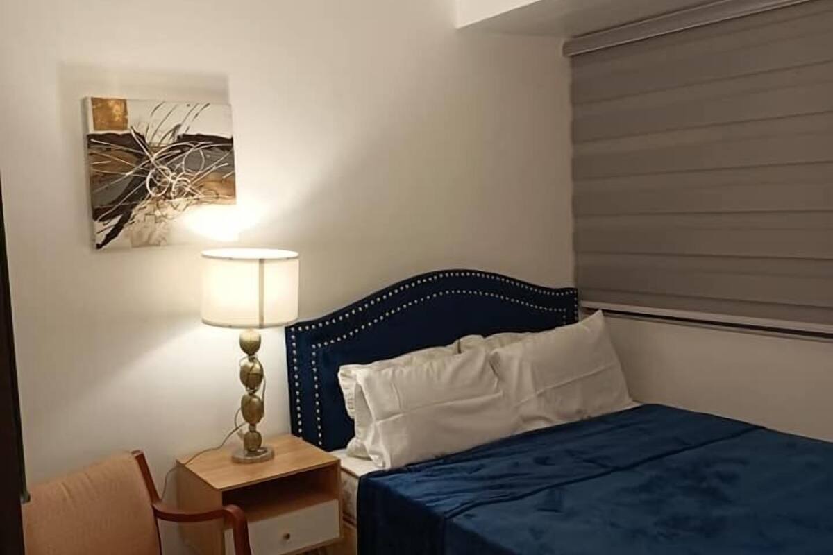 A bedroom with a bed, a chair, a nightstand, a lamp, and a painting on the wall.