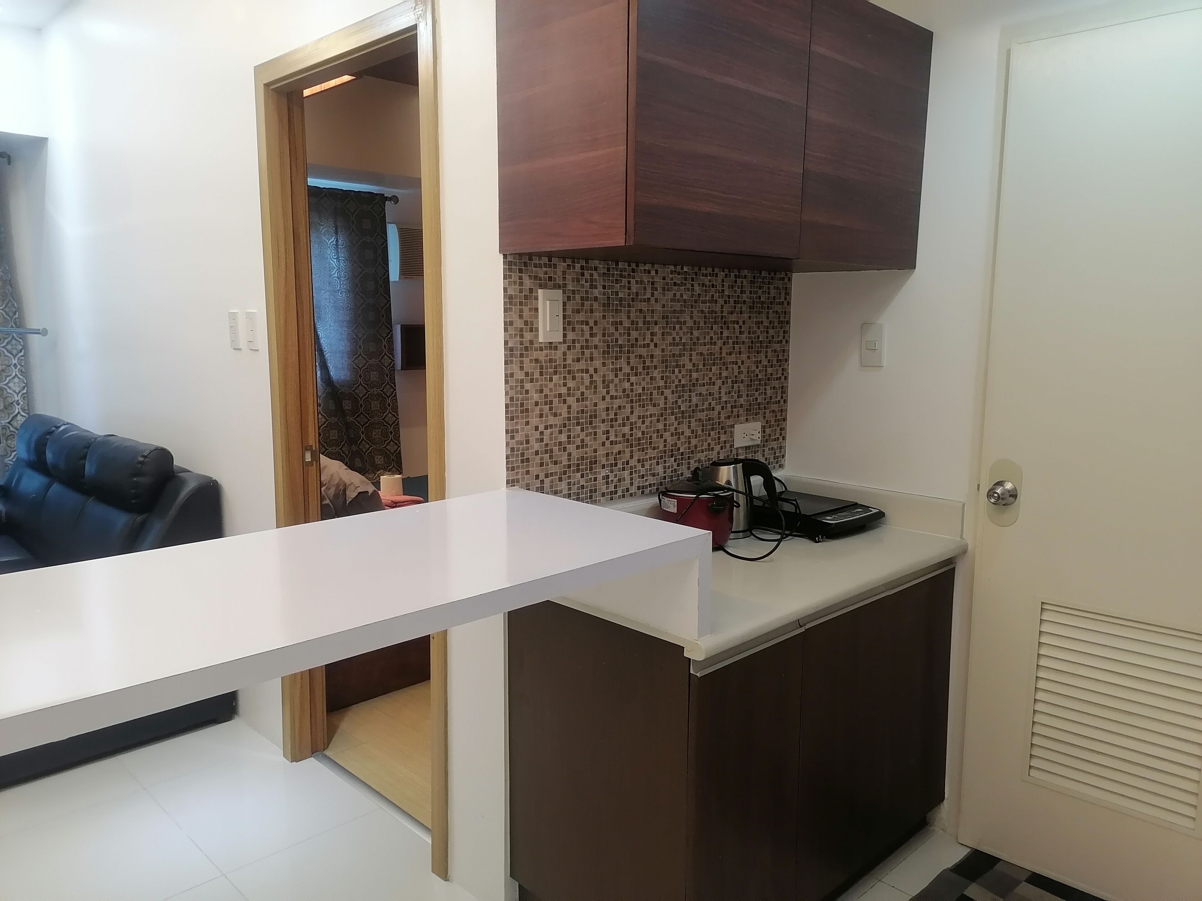 A compact kitchen with a white countertop, a microwave, and a red electric kettle.
