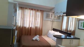 A hotel room with a bed, a desk, a chair, a mirror, and a window with curtains.