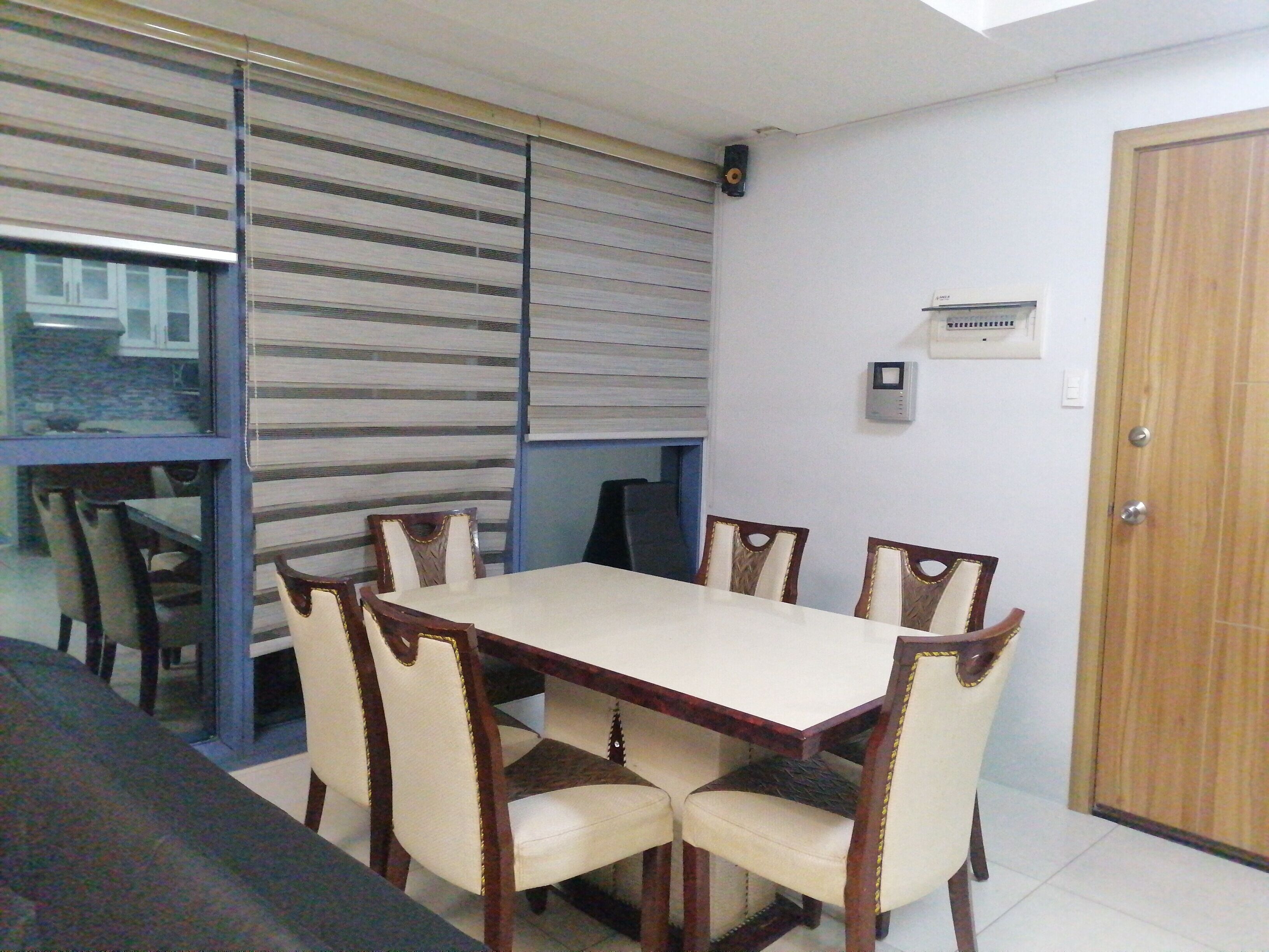 A dining area with a rectangular table and six chairs, a sliding glass door, and a thermostat on the wall.