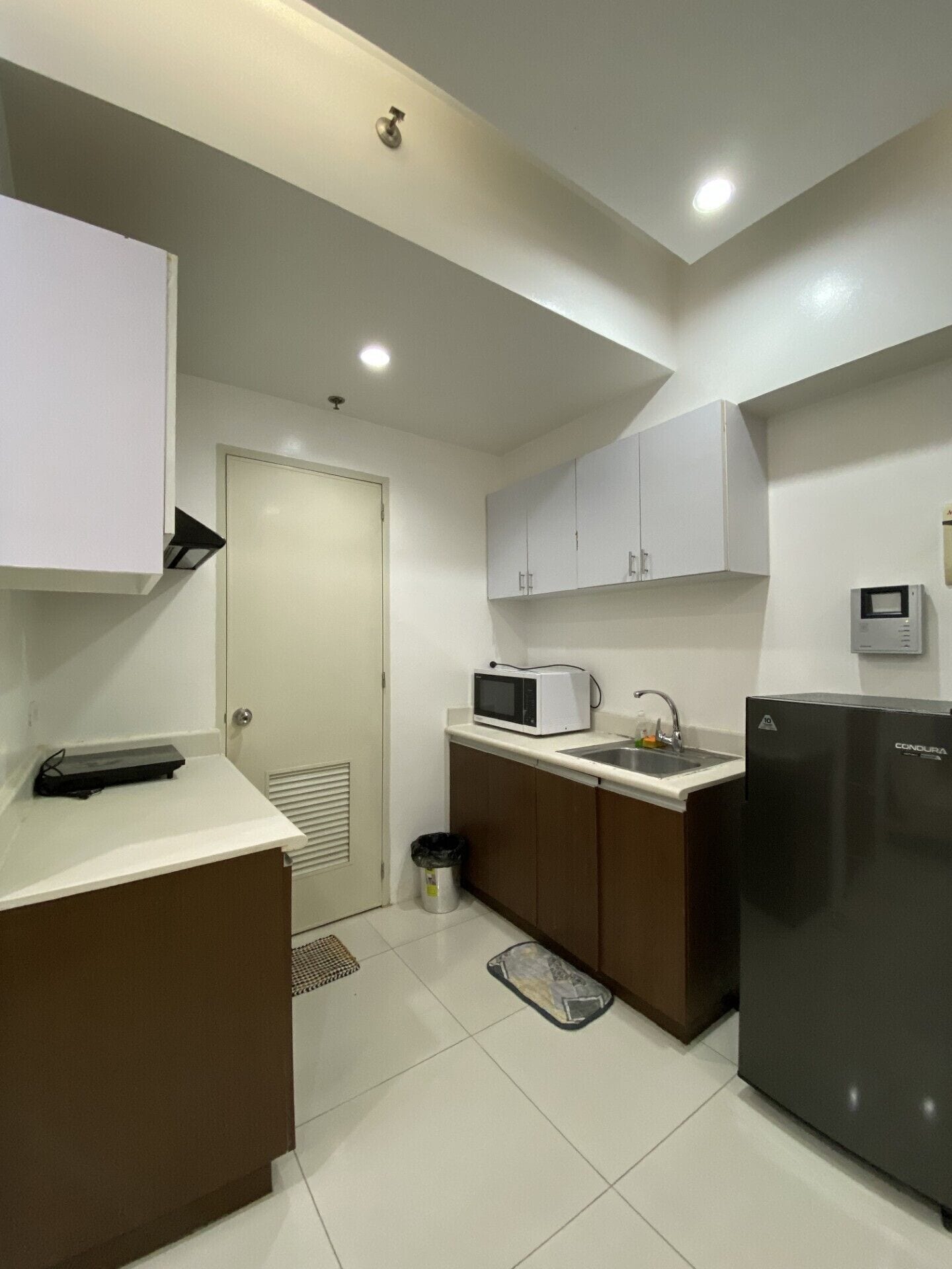 A compact kitchen with white cabinets, a microwave, a sink, and a refrigerator.
