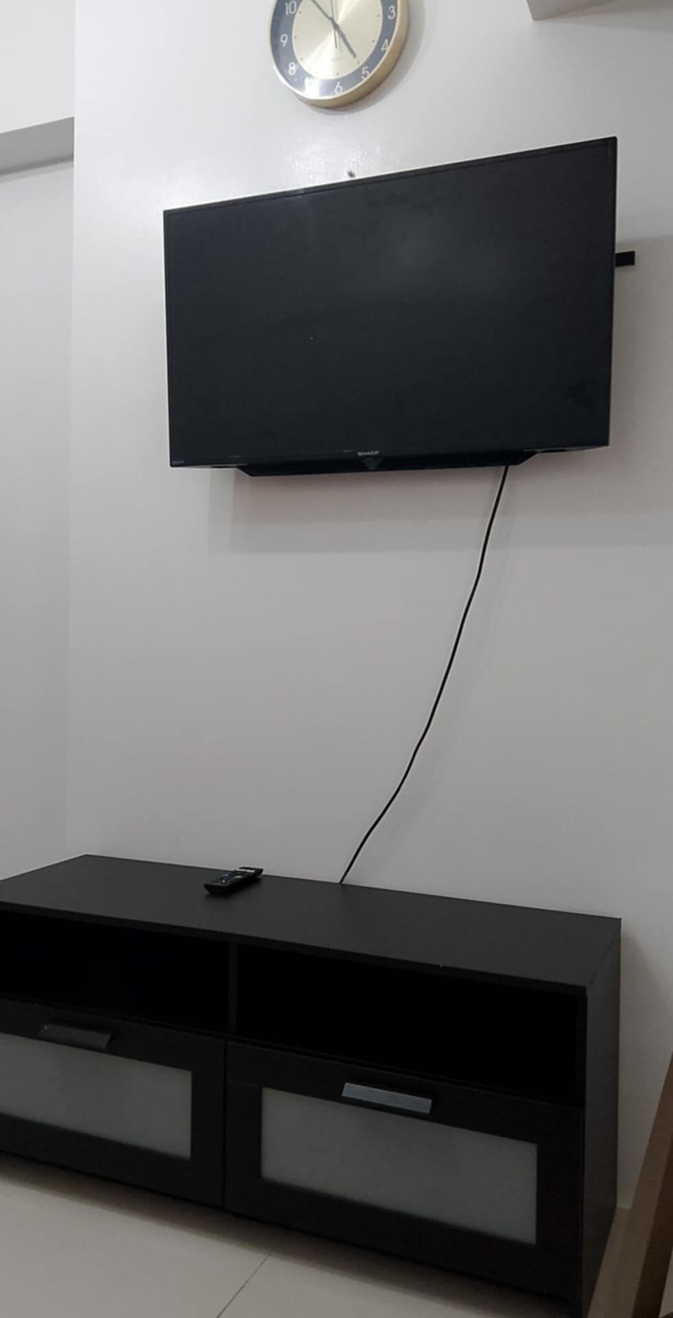 Una televisione a schermo piatto fissata a una parete bianca, collegata a un mobile contenitore nero con cassetti.