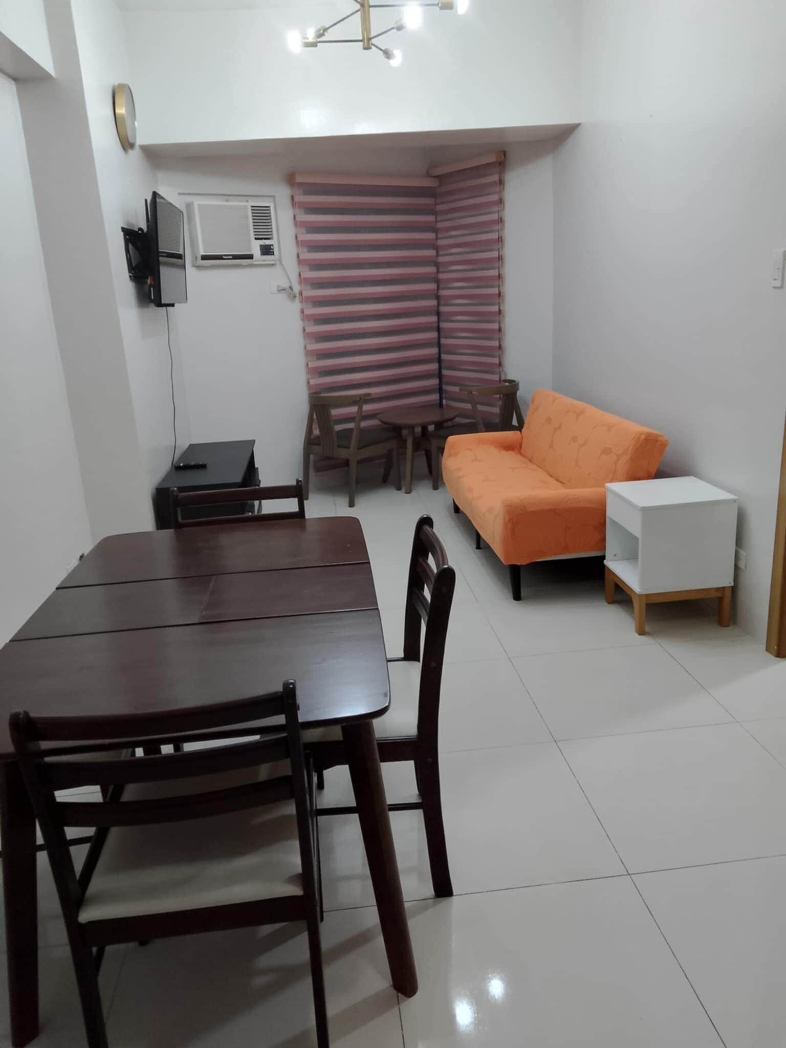 A compact living space with a dining table, chairs, a sofa, and a TV mounted on the wall.