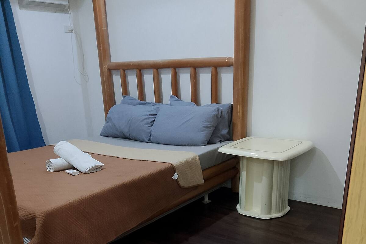 A single bed with a wooden headboard, a small bedside table, and a wall-mounted air conditioning unit.