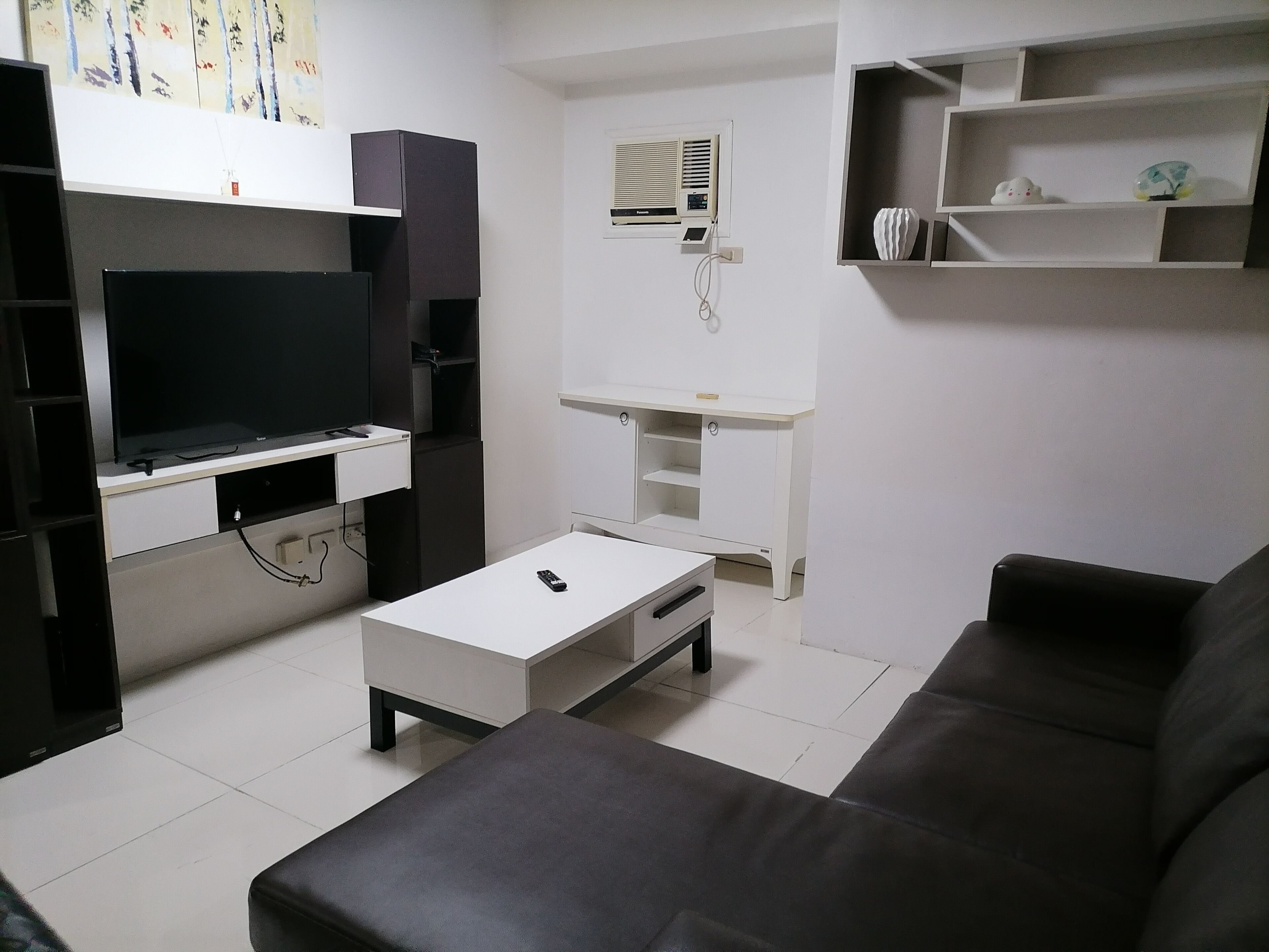A modern living room with a flat-screen TV, a white coffee table, a black sofa, and a white entertainment unit with shelves.