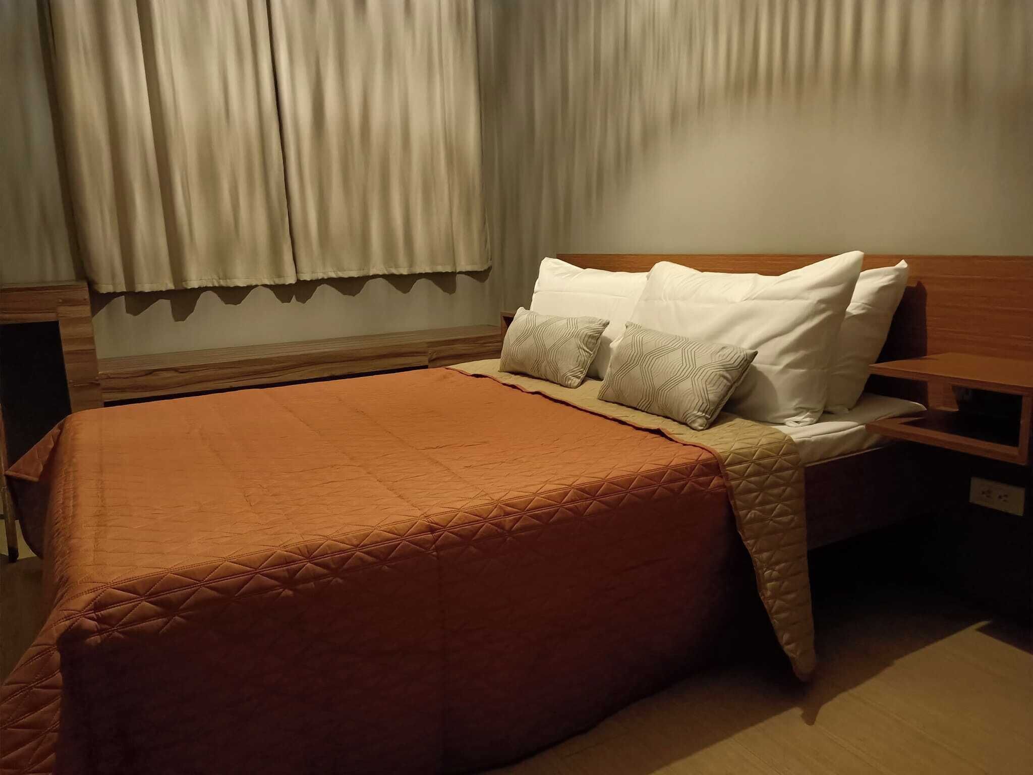 Un letto rifatto con un copriletto marrone, cuscini bianchi e una testiera in legno.