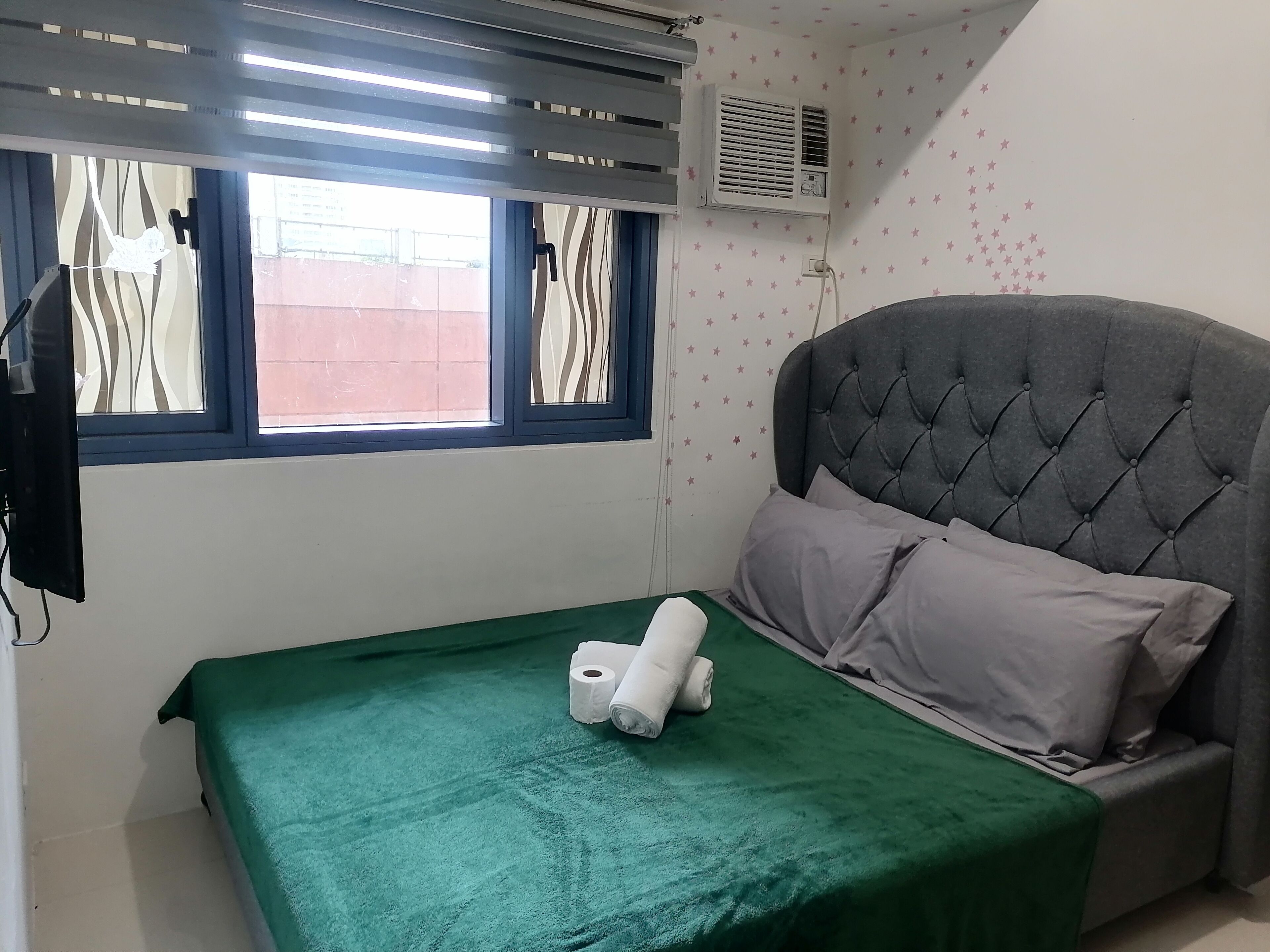 Un dormitorio con colcha verde, cabecera tapizada gris y dos almohadas.