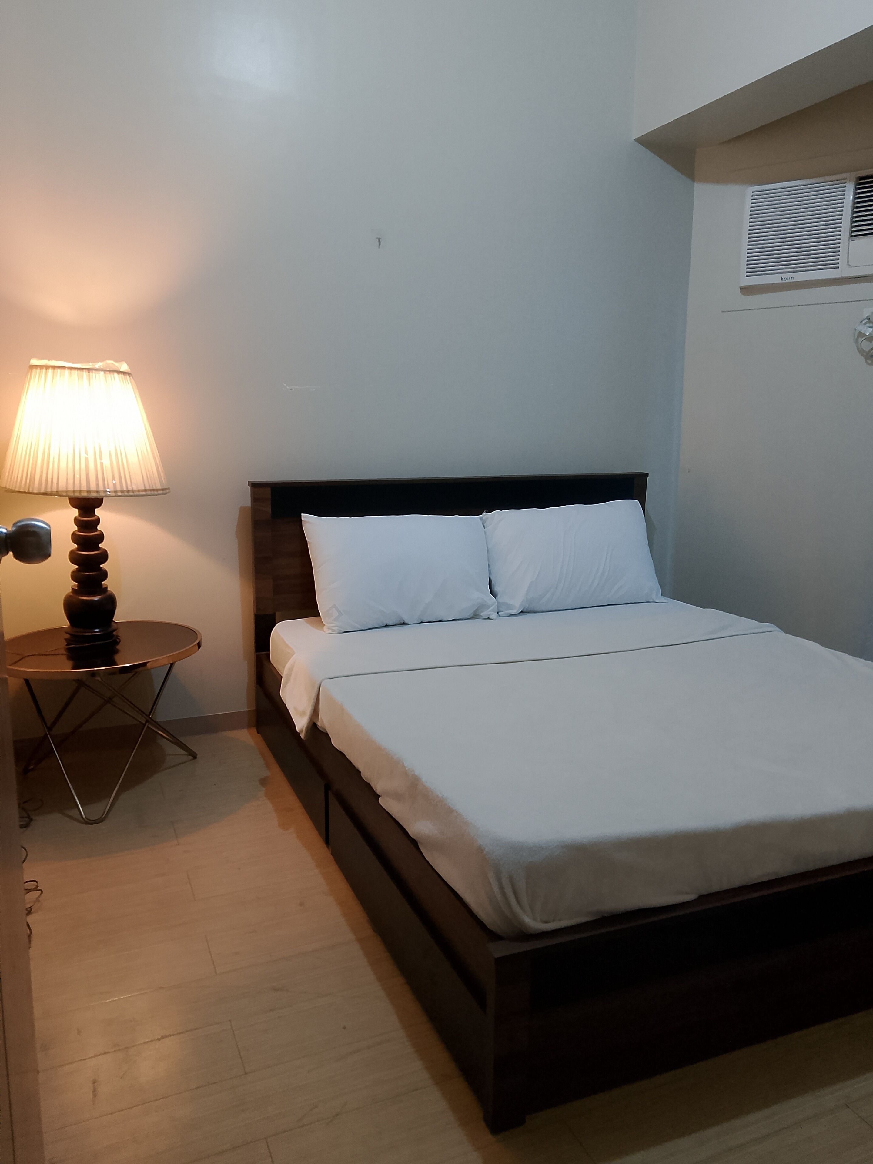 A bedroom with a bed, a bedside table with a lamp, and a wall-mounted air conditioner.