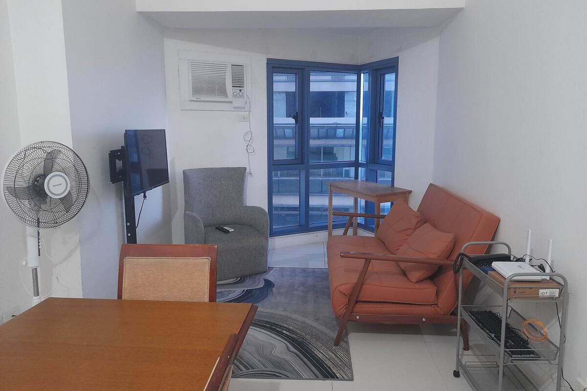 A compact living space with a sofa, a chair, a small table, a fan, and a TV.