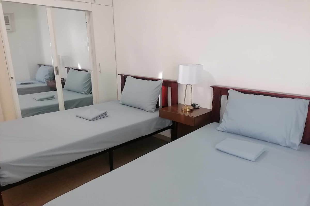 A hotel room with two single beds, a nightstand with a lamp, and a mirror on the wall.