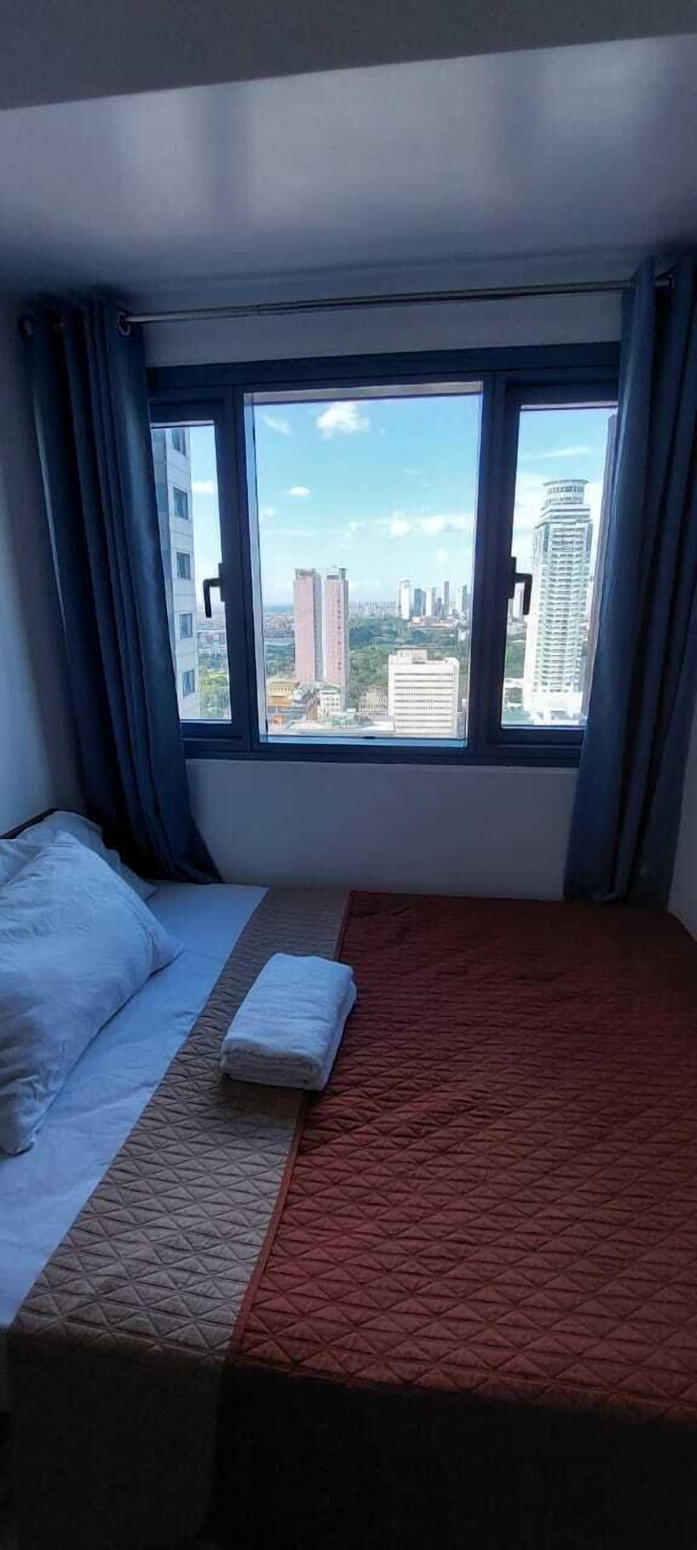 A hotel room with a bed, a window with curtains, and a view of a cityscape.