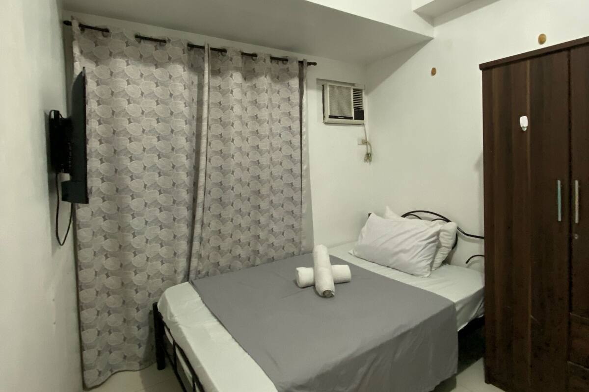 A small, well-lit bedroom with a single bed, a wardrobe, and a curtain.