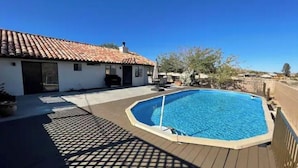 A swimming pool with a tiled deck, a house with a red-tiled roof, and a clear blue sky. - The Peaceful Retreat (5 min from the park entrance w/ Pool! (Joshua Tree)