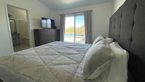 A bedroom with a large bed, a ceiling fan, a dresser, and a view of a swimming pool. - The Peaceful Retreat (5 min from the park entrance w/ Pool! (Joshua Tree)