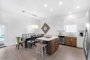A modern kitchen with a central island, wooden cabinets, and a dining area with a chandelier. - Epic! Ocean views! Sleeps 20! Pool! Golf cart! (Destin)
