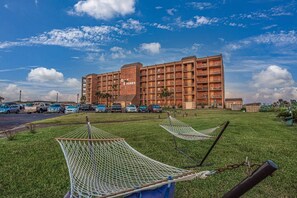 Un hotel con varios balcones, estacionamiento y un espacio con césped y hamacas.