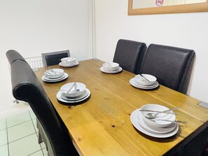 A dining area with a table set for six, featuring a white plate, fork, and spoon at each place setting.