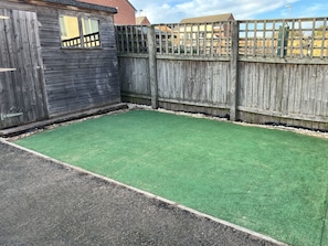 Backyard with artificial turf and a wooden fence, featuring a deck beyond.