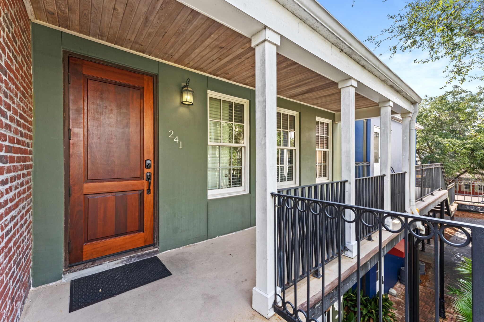 A house with a green exterior, a wooden front door, and a porch with a black railing.