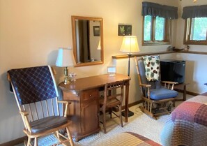 Een gezellige kamer met een houten bureau, twee stoelen, een spiegel, een lamp en een televisie.
