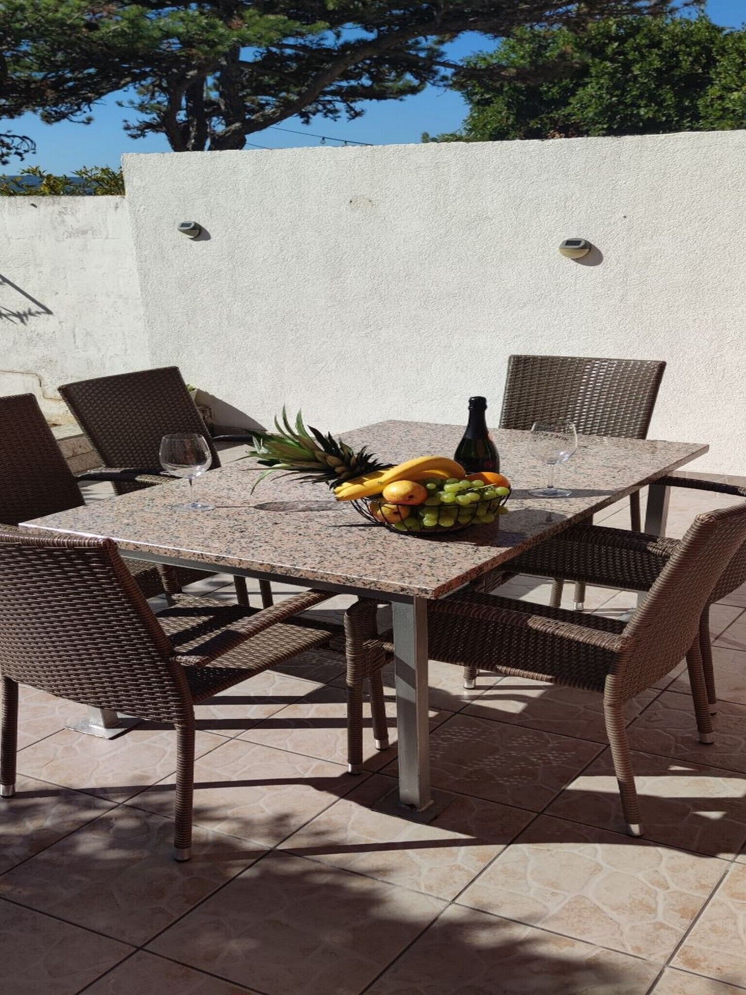 Een terras buiten met een tafel voor twee personen, rieten stoelen en een fruitmand.