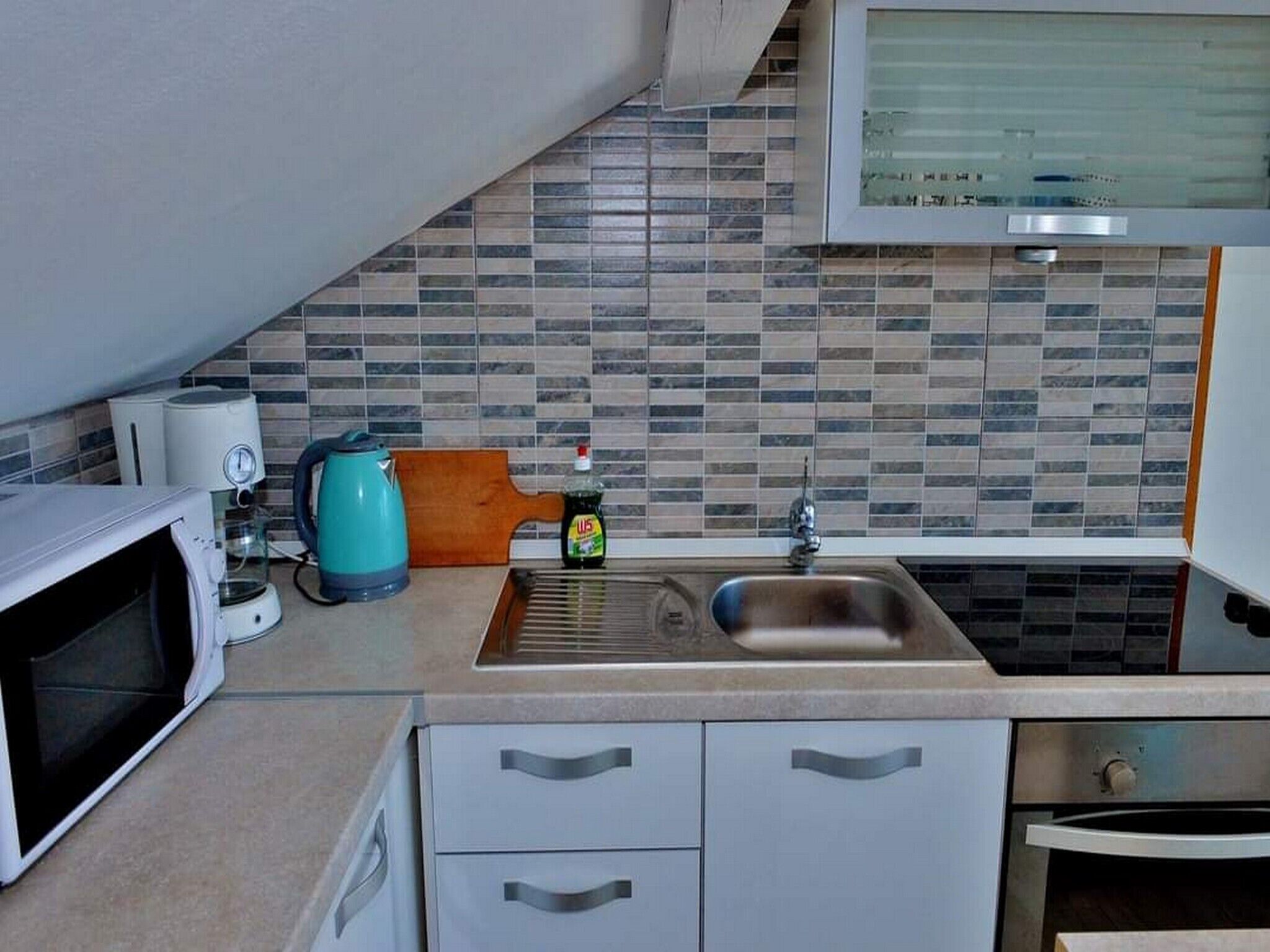 Een kleine keuken met een magnetron, waterkoker en wastafel.