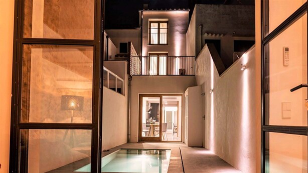Ein modernes Gebäude mit Pool in Glasfassade, Balkon im zweiten Stock und einem gut beleuchteten Eingang.