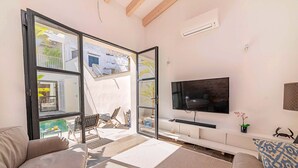 Ein modernes Wohnzimmer mit einer großen Schiebeglasdoor zum Balkon, einem Wand-Fernseher und einem Sofa mit gemustertem Kissen.