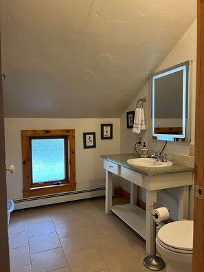 Un bagno piccolo e luminoso, con finestra, lavandino, WC e specchio.
