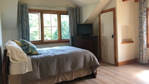 Une chambre à coucher avec un lit, un téléviseur posé sur une commode, une fenêtre avec des rideaux et une porte.