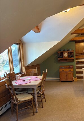 Zona pranzo con tavolo e sedie in legno, una finestra e un mobiletto in legno con stoviglie.